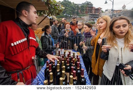 TBILISI, GEORGIA - OCT 16, 2016: Women tasting wine with bartender in national georgian costume at festival Tbilisoba on October 16, 2016. Tbilisoba is traditional festival in capital of Georgia from 1979