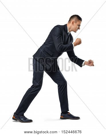 Young businessman posing like he is pulling a rope over his shoulder isolated on a white background. Making efforts. Working hard. Dragging and overcoming something.