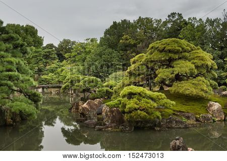 Kyoto Japan - September 19 2016: View on part of the garden of Ninomaru Palace at Nijo Castle. Pond rocks trees and a small bridge. Cloudy sky.
