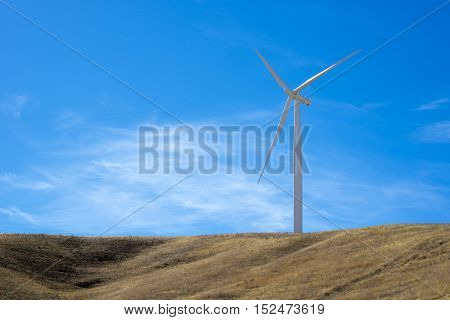Single wind turbine on top of a hill with blue sky