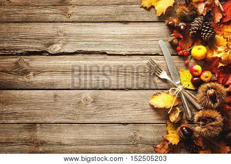 Vintage autumn border from fallen leaves and fruits with vintage silverware on wooden table. Thanksgiving autumn background
