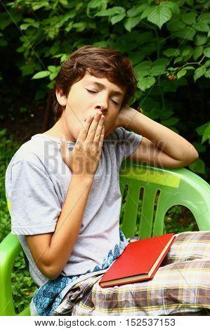 boy with book yawning close up photo in the summer garden. Boy yawn.