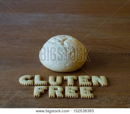 A gluten free bread roll, bap or bun with the phrase Gluten Free spelled out using alphabet shaped cookies on a wooden background.