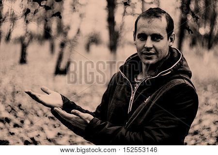 Happy smiling man in a jacket, presenting and showing something on the background of nature