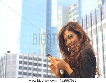 Portrait of Asian business woman on black dress use moblie with tower background