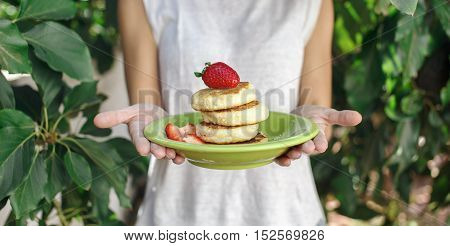 Sweet ricotta pancakes in a plate with strawberry in woman hands summer day in the garden. Eating concept.