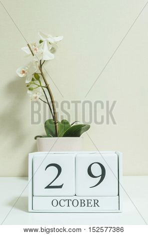 Closeup white wooden calendar with black 29 october word with white orchid flower on white wood desk and cream color wallpaper in room textured background selective focus at the calendar