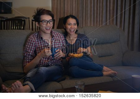 Asian young couple watching comedy movie on tv at night