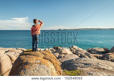 Boy standing at the edge of the rock and looking into the sea at Port Elliot South Australia. Color toning applied