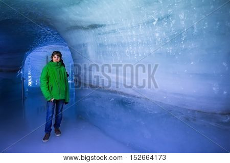 Child visiting ice cave tunnel in Swiss Alps glacier. School kid walking in ice tunnel in the mountains. Beautiful view of Aletsch glacier Switzerland. Tourist on winter vacation.
