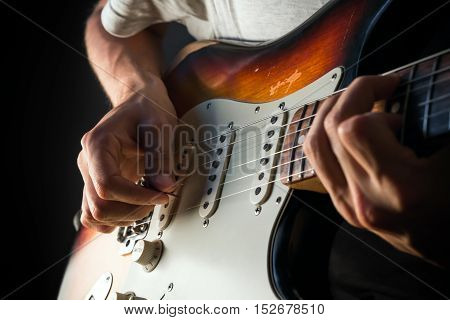 Vintage electric guitar closeup, male hands playing with a pick. Closeup photo of male hands playing vintage electric sunburst guitar with mint pickguard with pick in front of dark background.