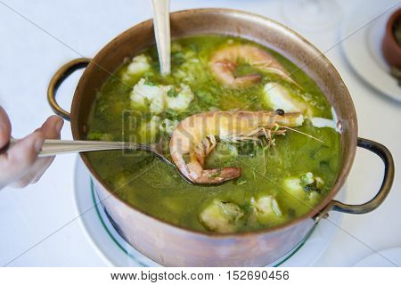 Arroz de Tamboril or soupy seafood rice portuguese recipe. Hand holding the spoon with a prawn