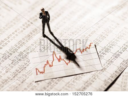 Model figure stands on rate tables and looks skeptically on a graph with stock prices.