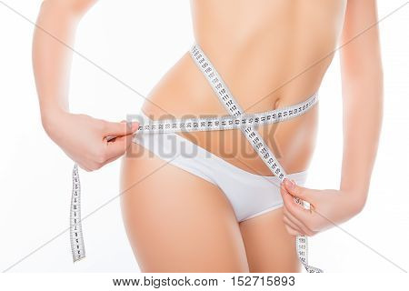 Close up photo of healthy woman with slim belly measuring her waist's size