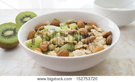 Whole grain cereal with kiwi and almond in white bowl and yogurt. Healthy breakfast. Health and diet concept selective focus close up horizontal