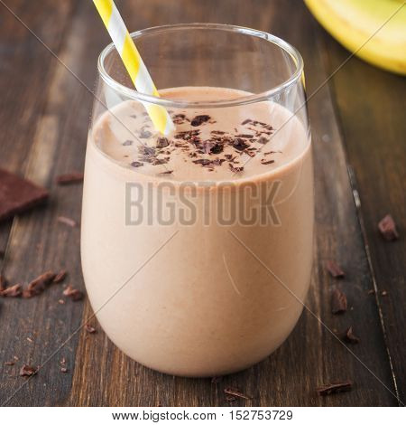Chocolate banana smoothie in glass with paper straw on wooden background selective focus