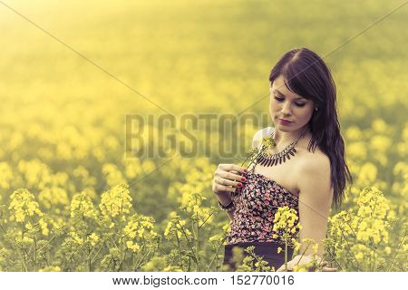 Beautiful woman in meadow of yellow flowers with glimps down. Attractive happy young girl enjoying the warm summer sun and her health in a wide green and yellow meadow. Part of series.