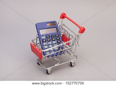 Calculator in shopping trolley cart isolated on gray. Financial concept.