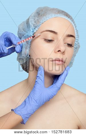 Attractive young woman gets cosmetic injection an injection in the upper lip over blue background. Doctors hands making an injection in face close-up. Beauty Treatment. injection in the eyelid
