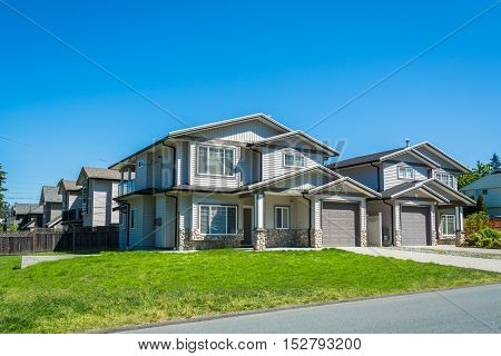 Residential duplex building with concrete drive ways and green lawns in front. Two family dwelling with asphalt road in front