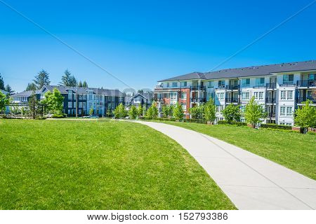 Concrete pathway across huge green lawn in front of residential condo building. Apartment building on sunny day with blue sky.