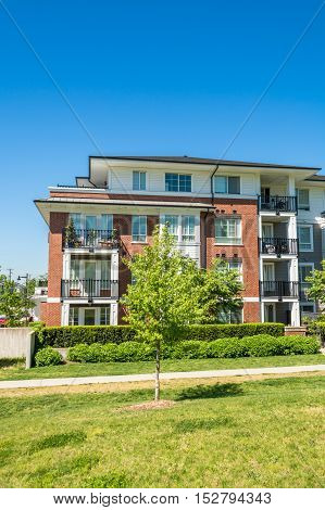 Brand new low rise apartment building with concrete pathway and small tree in front on sunny day in British Columbia Canada