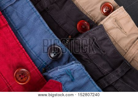 Fragment Of Four Cotton Twill Pants Red, Blue, Black, Beige With Open Buttons. Close Up.