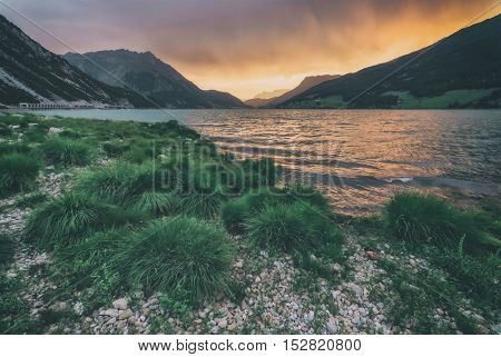 Beautiful view of the lake Resia. Dramatic sky and colorful sunset. Alps, Italy, Europe, toned like Instagram filter
