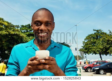African american man sending message with phone outdoor in the city in a warm cinema look