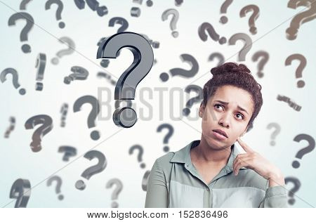 African American girl standing in gray room with floating question marks in the background. Concept of decision making. Toned image