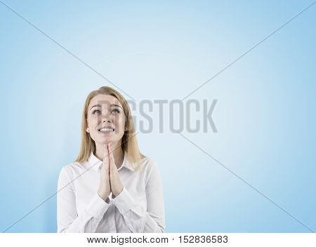 Woman hoping for the best is standing with her palms together against blue background. Concept of hope. Mock up