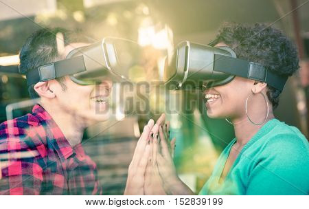 Multiracial couple in love going beyond racial diversity through virtual reality glasses - Young people having fun using new technology - Composition with window reflection on enhanced sun flare halo