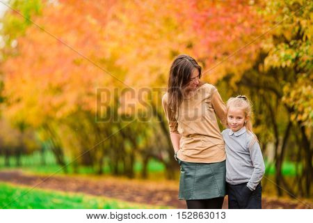 Young mother with cute little girl in autumn park on sunny day