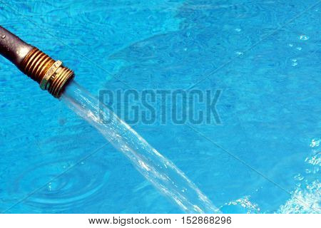 Close-up of garden hose water filling crystal blue water in swimming pool on bright hot summer day