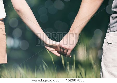 Young couple holding hands together on blurred nature background