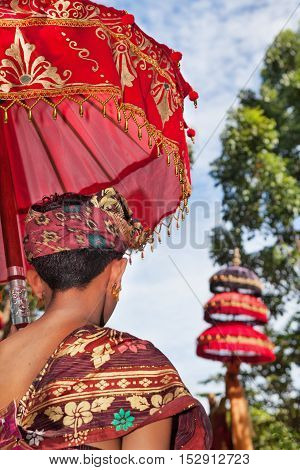 Balinese man in sarong costume hold red umbrella with traditional pattern on ceremony in hindu temple. Arts festivals in Indonesia culture of Bali island Indonesian people. Asian travel background