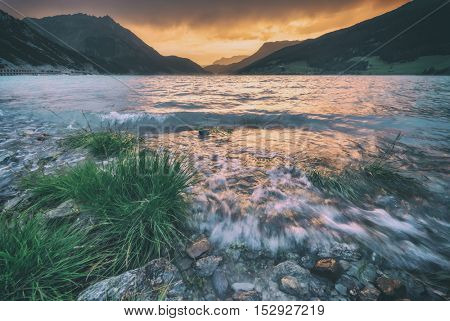 Beautiful view of the lake Resia. Dramatic sky and colorful sunset. Alps, Italy, Europe. Toned like Instagram filter