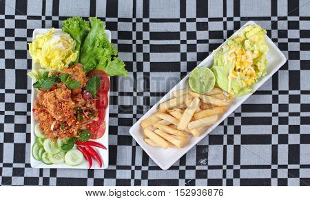 Spicy sour fried chicken salad (Yum Kai Zap in Thai) served with a dish of mixed vegetables salad and french fires.