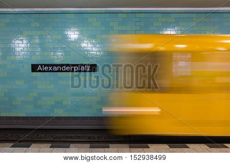 Yellow subway train in Motion. Berlin Alexanderplatz sign visible on the wall of underground station.