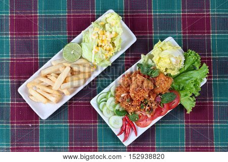 Spicy sour fried chicken salad (Yum Kai Zap in Thai) served with a dish of mixed vegetables salad and french fires.
