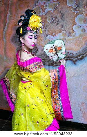 beautiful chinese woman standing in a half-turn in the yellow Chinese national traditional dress with fan