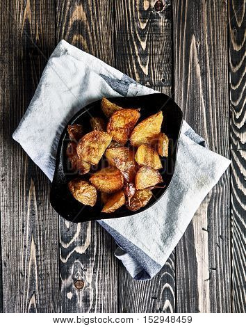 Delicious baked potato wedges with garlic with husk in black rustic plate on dark wooden table. Appetizing crisp. Traditional garnish or side dish for Christmas dinner. Country-style roasted potatoes