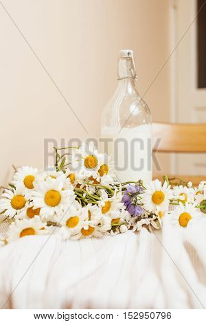 Simply stylish wooden kitchen with bottle of milk and glass on table, summer flowers camomile, healthy foog moring concept noone