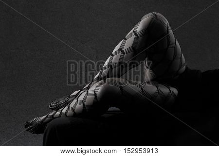 Low key grey scale photo of sexy female nude legs in net tights against dark background with copy space horizontal view