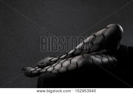 Low key grey scale photo of sexy female nude legs in net tights against dark background with copy space horizontal view