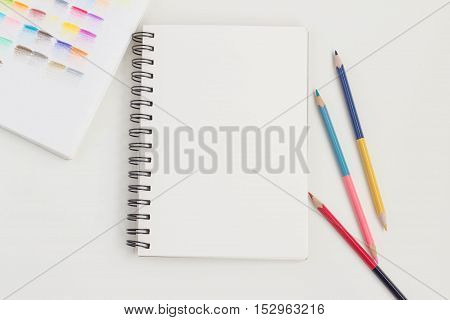 Top view of art supplies on white table. Colored pencils, paintbrushes and sketchbook.  May be used as product mockup.