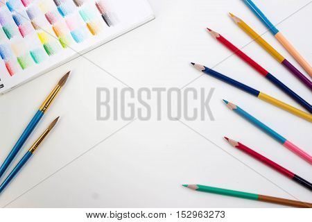 Top view of art supplies on white table. Colored pencils, paintbrushes and sketchbook.  May be used as product mockup.