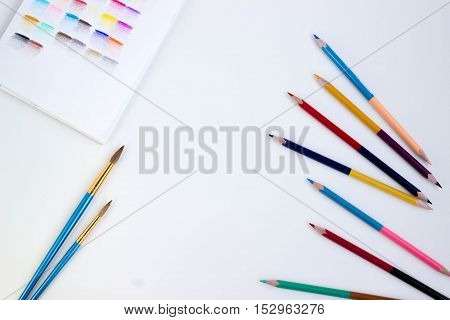 Top view of art supplies on white table. Colored pencils, paintbrushes and sketchbook.  May be used as product mockup.
