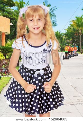 Beautiful little blonde girl in polka dot dress, the girl upset. Close-up.On the background of the road on which the tourists leave.