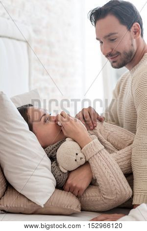 Care and love. Good looking cheerful young man sitting near his wife and smiling while looking at her